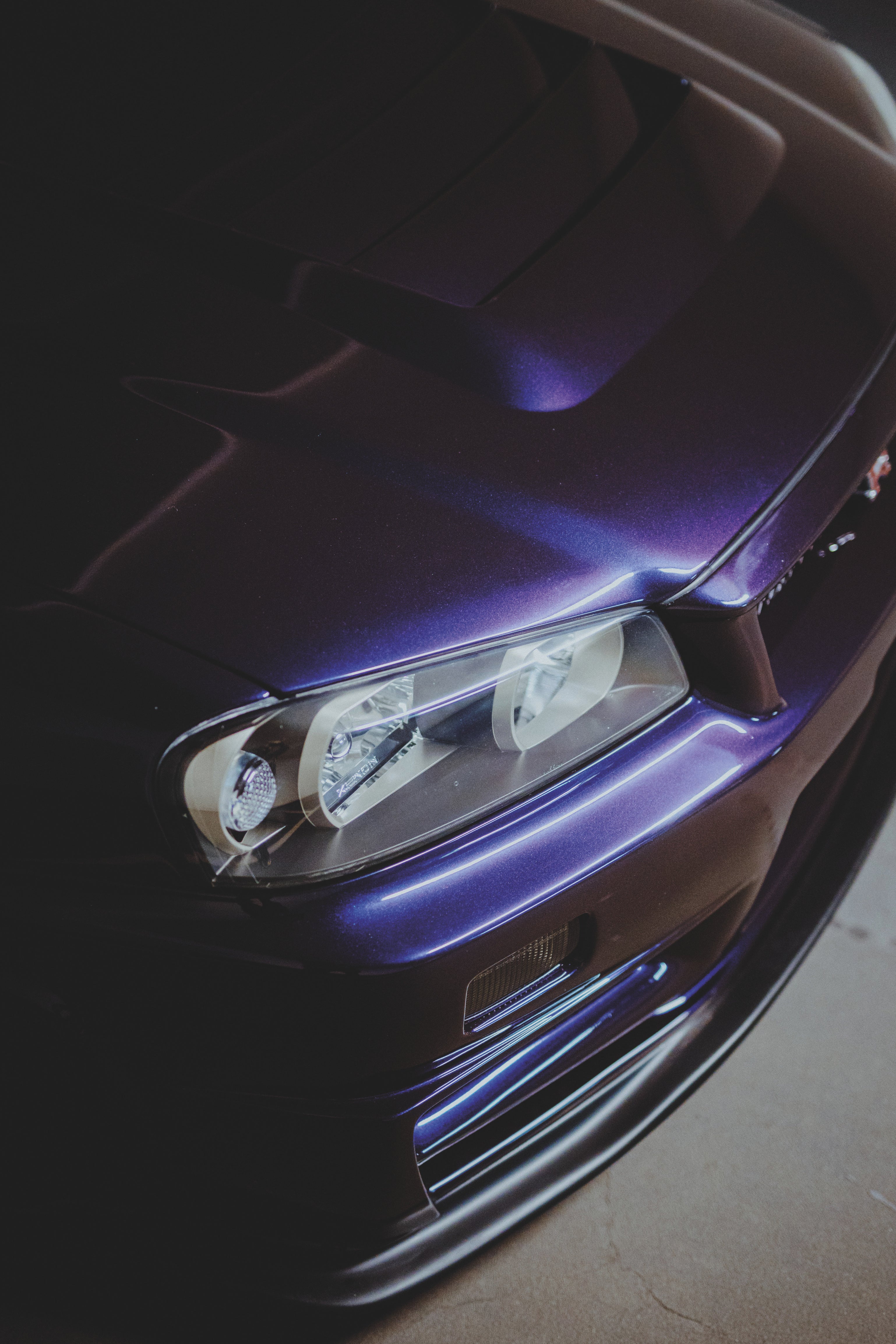 Schräger Blick von oben auf Scheinwerfer, violette Motorhaube und Frontstoßfänger eines Nissan Skyline R34.