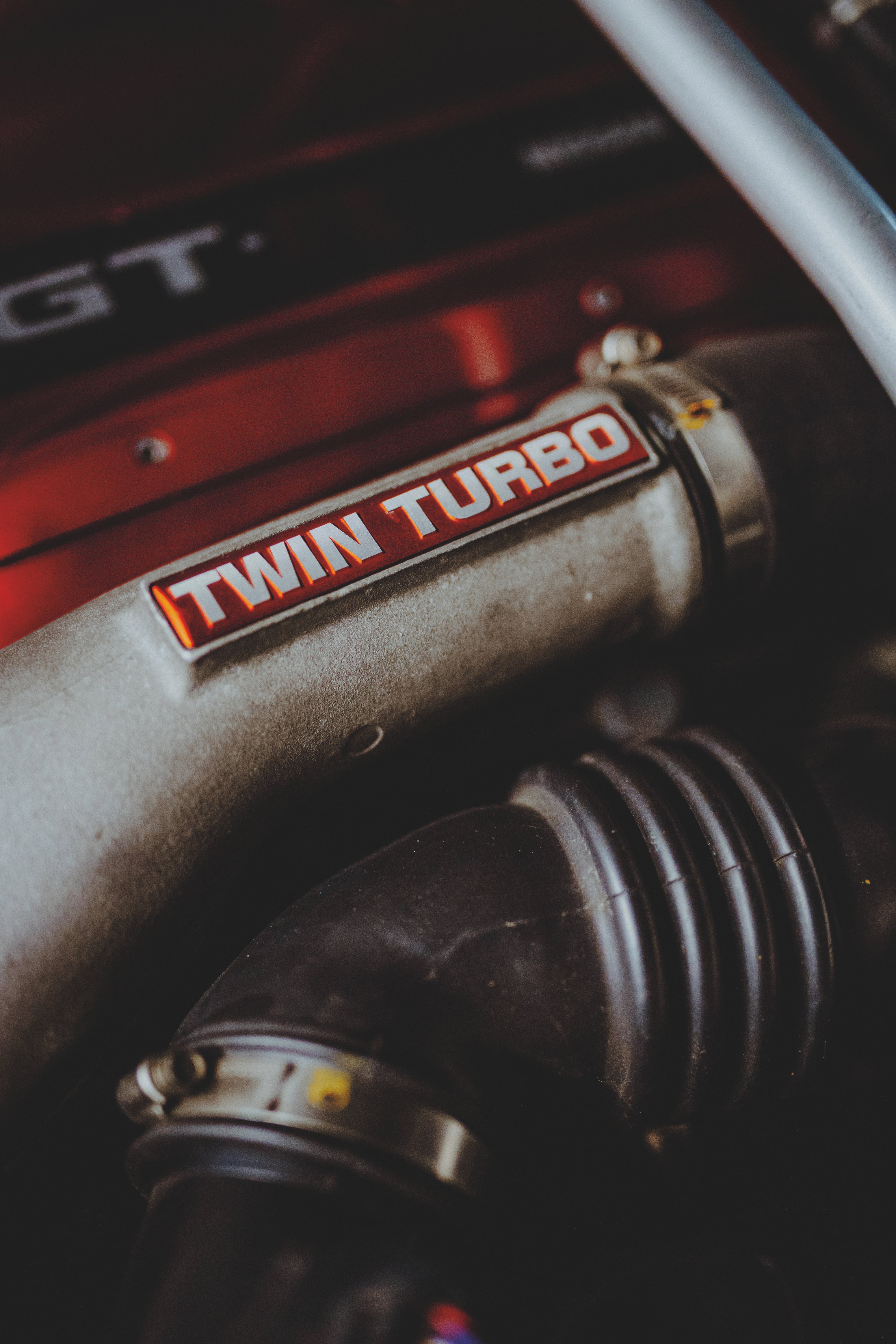 Motorraumdetail mit rotem Bauteil, silbernem Rohr mit Twin-Turbo-Schriftzug und schwarzem Schlauch.