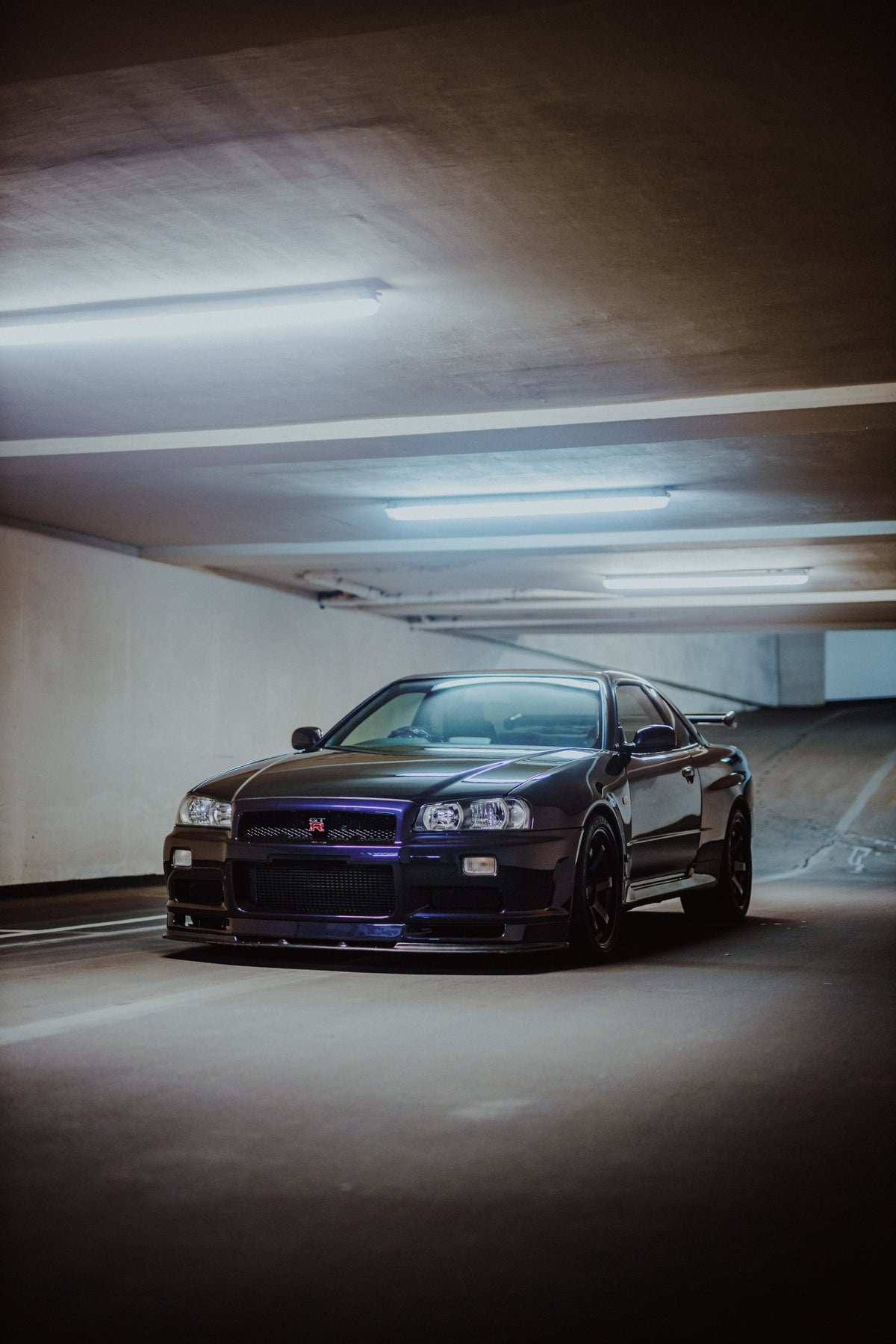 Nissan Skyline R34 schräg von vorn mit viel sichtbarer Betondecke und Garagenboden.