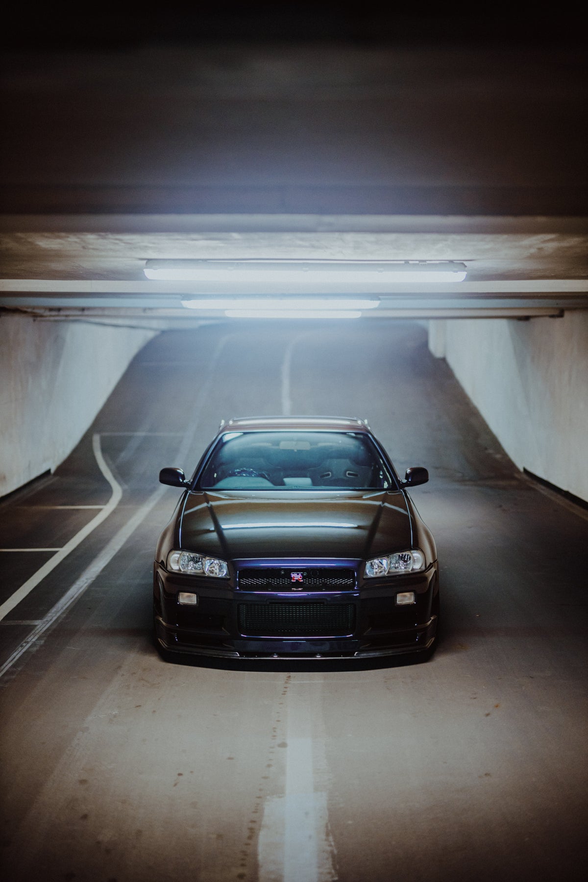 Nissan Skyline R34 frontal aus erhöhter Perspektive zwischen den Wänden einer Tiefgaragenrampe.
