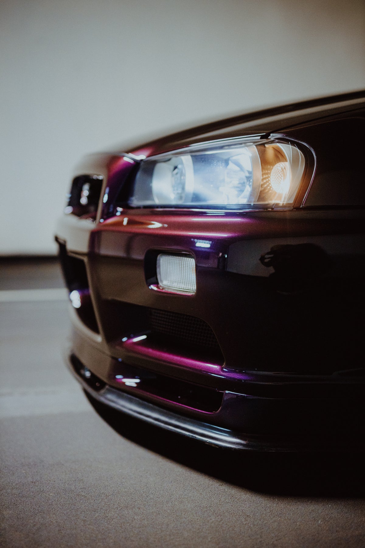 Nahaufnahme von Scheinwerfer, Zusatzleuchte und violettem Frontstoßfänger eines Nissan Skyline R34.