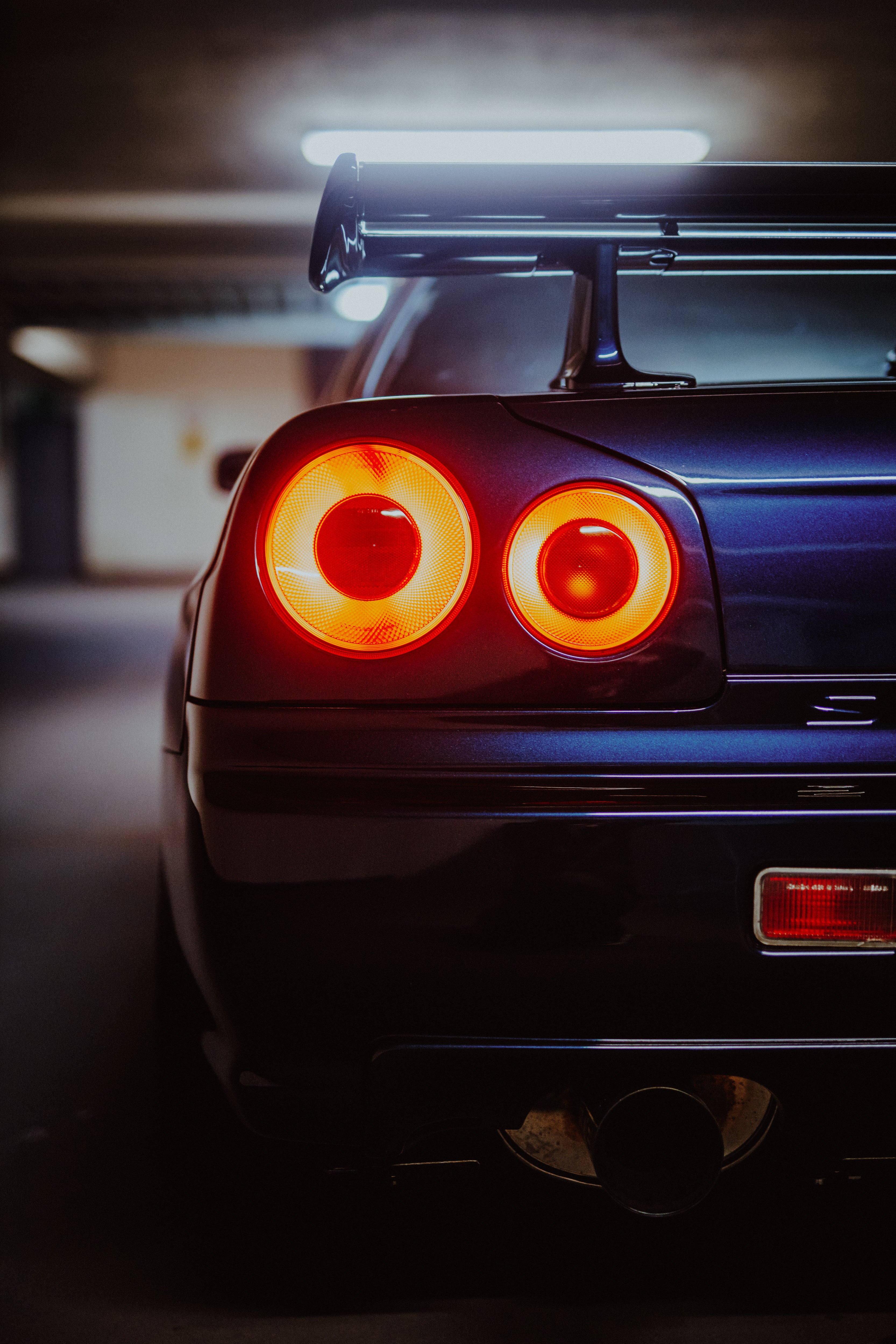 Nahaufnahme zweier leuchtender runder Rückleuchten eines Nissan Skyline R34 mit Heckflügel und Stoßfänger.