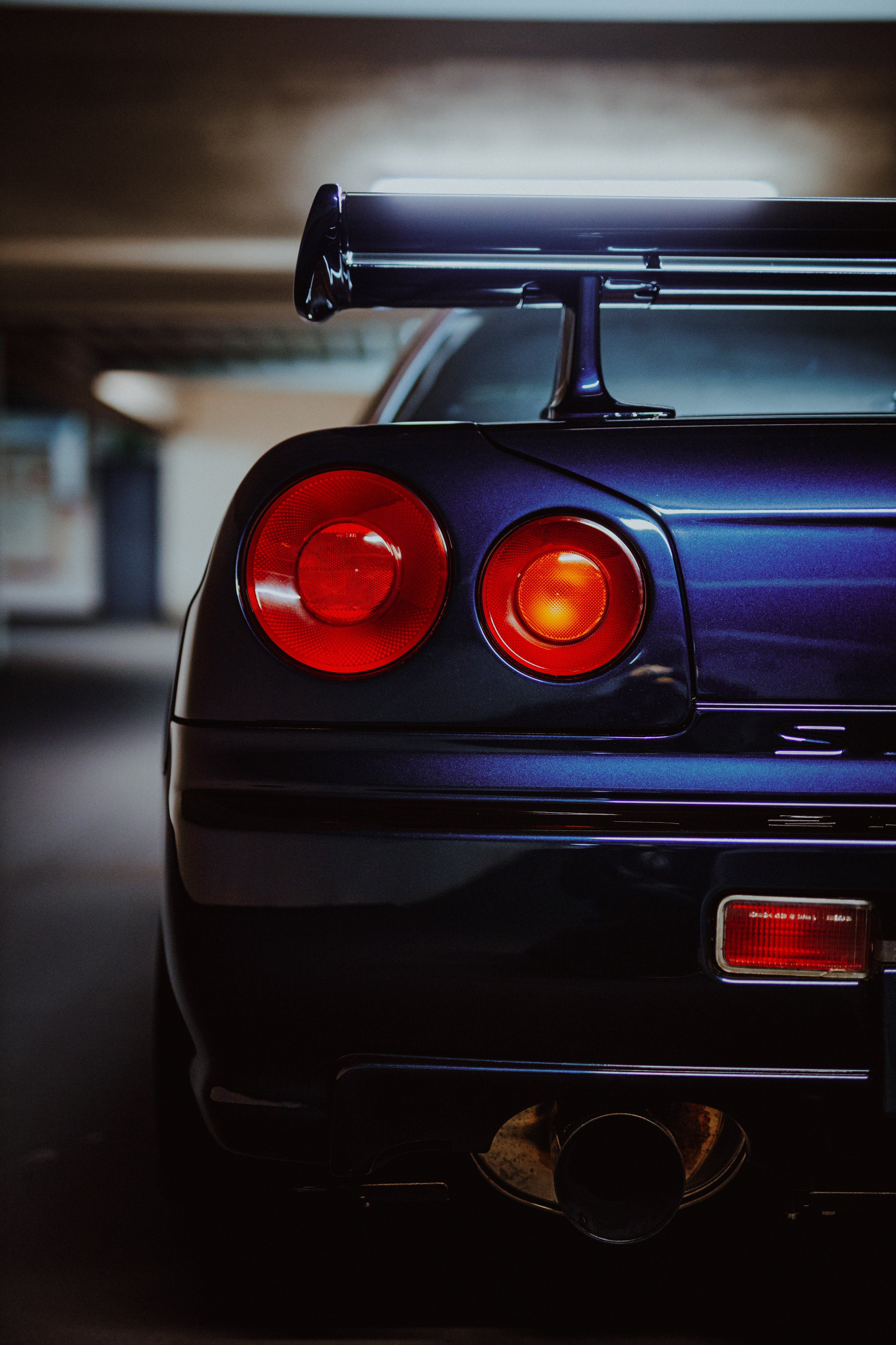 Nahansicht der Heckpartie des Nissan Skyline R34 GT-R MNPII mit zwei runden roten Rückleuchten und Heckflügel.