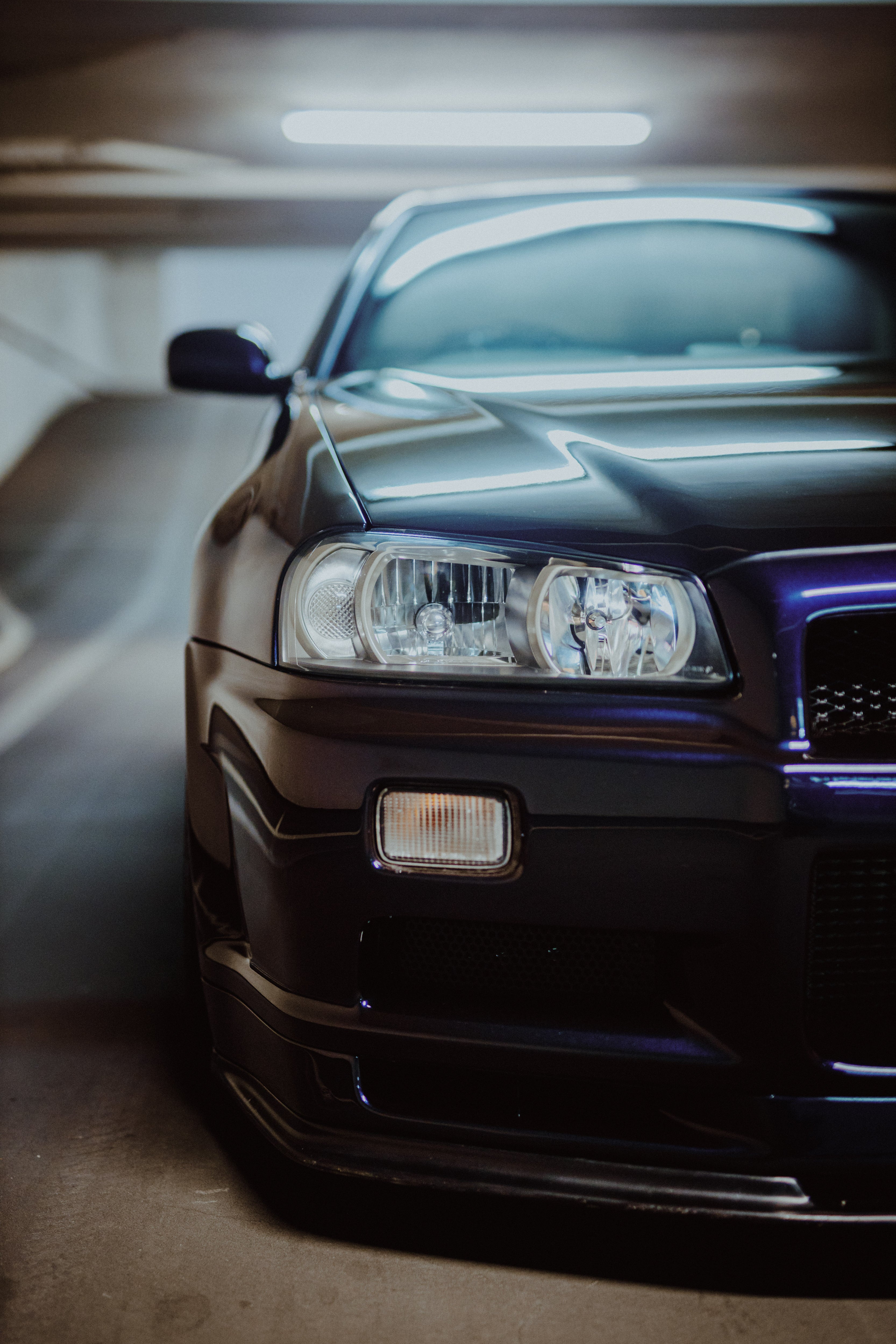 Nahaufnahme einer Frontseite des Nissan Skyline R34 mit Scheinwerfer, Motorhaubenkante und Stoßfänger in einer Tiefgarage.