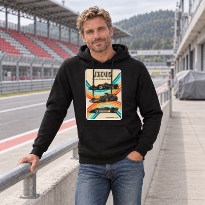 Mann im schwarzen Hoodie am Geländer einer Rennstreckentribüne. Vorn zeigt der Hoodie eine helle LEGENDS-Grafik mit drei Rennwagen und geschwungenen Farbbändern.