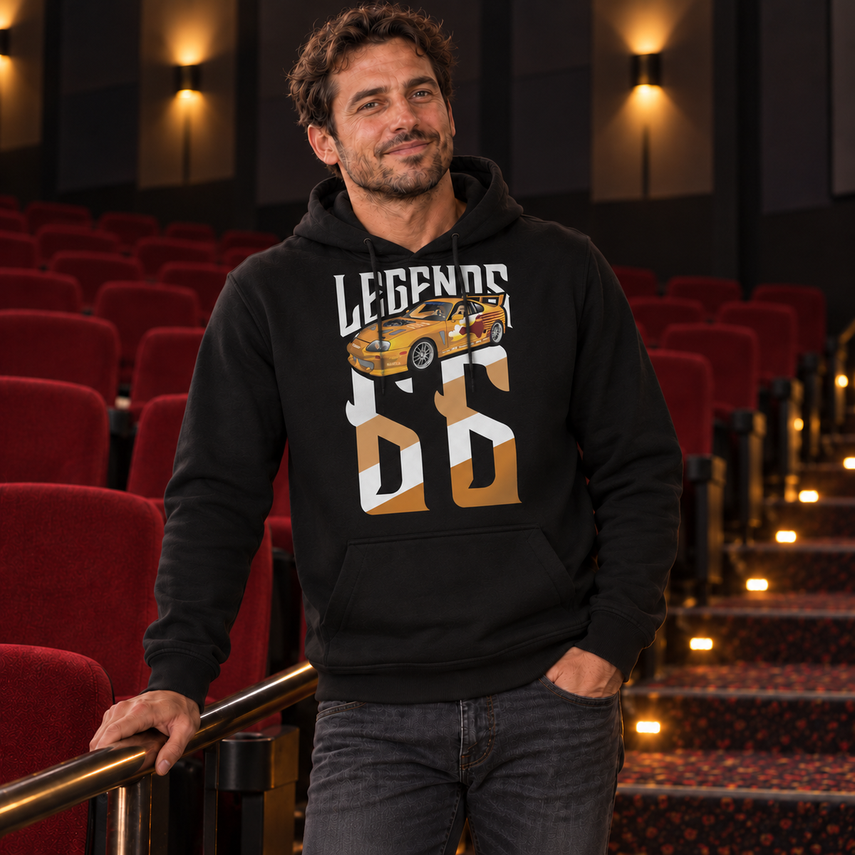 Mann im schwarzen Hoodie mit Slap Jack’s Supra als Legends-Frontmotiv steht am Geländer im Kinosaal mit roten Sitzen.