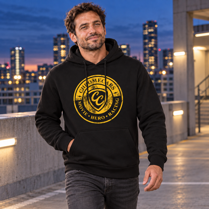 Ein Mann geht auf einem Parkdeck vor beleuchteten Hochhäusern. Er trägt einen schwarzen Hoodie mit gelbem Stempelmotiv auf der Brust und hält eine Hand in der Kängurutasche.