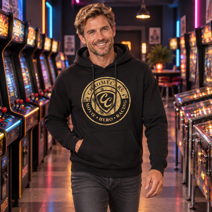 Ein Mann im schwarzen Hoodie mit goldfarbenem CC-Stempelmotiv steht frontal im Gang einer Retro-Spielhalle, eine Hand in der Kängurutasche und den anderen Arm seitlich gesenkt.