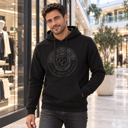 Ein Mann im schwarzen Hoodie mit dezentem schwarzem ChromeCars-Stempelmotiv steht vor einem Schaufenster im Shoppingcenter, eine Hand in der Kängurutasche, den anderen Arm gesenkt.