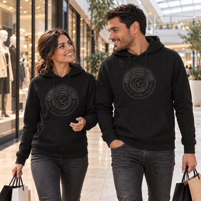 Eine Frau und ein Mann gehen in schwarzen Hoodies mit schwarzen Stempelmotiven nebeneinander durchs Shoppingcenter und sehen einander an. Beide tragen Einkaufstüten; die Frau hebt ihre freie Hand vor den Körper.